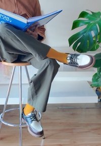 Footwear with a metallic silver upper, brown accents, and white sole. Paired with bright orange ribbed socks and olive green trousers.