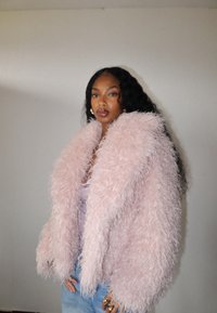 Puszysta, oversize różowa kurtka wykonana z teksturowanego materiału, z wysokim kołnierzem i pełnymi rękawami, noszona na jasnofioletowej bluzce.