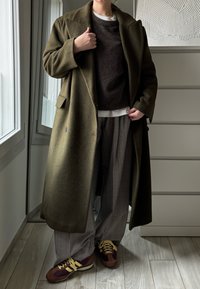Olivgrüner Wollmantel, brauner Pullover, graue kariertes Hosen, und burgunderrote Sneakers mit gelben Akzenten. Glatte Textur, oversized Silhouette.