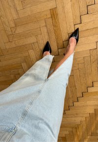 Svetlo modra denim krila z bočnim razporkom, v kombinaciji s črnimi čevlji na visokih petah s koničastim nosom. Ozadje prikazuje leseno talno oblogo v ribji kost.