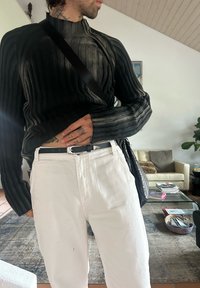 Czarny prążkowany sweter z wysokim kołnierzem, zestawiony z białymi spodniami i czarnym paskiem. Akcesoria to teksturowana torebka na ramię.