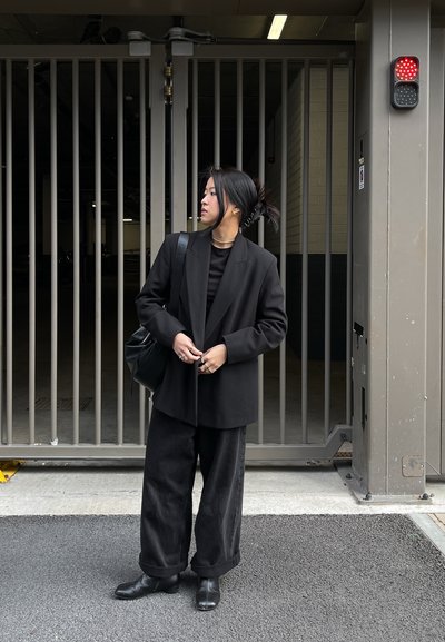 Blazer negro oversize, top negro, pantalones anchos negros y botines. Los accesorios incluyen un collar grueso y pendientes.