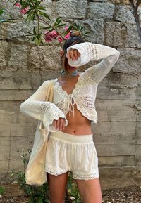 Bela kvačkana kratka majica s valovitim robom, zaveznim detajlom spredaj in rokavi v stilu zvončkov, v kombinaciji z belimi kratkimi hlačami z čipkastim robom. Nevtralna torba.