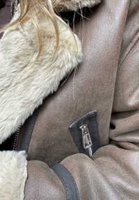 Smeđa jakna od ovčje kože s teksturiranim završetkom, sa mekanim krznom od umjetne kože na ovratniku i detaljima na prednjem dijelu sa zatvaračem.