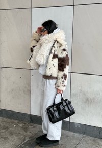 Dirbtinės kailio paltas su rudu ir balta dėmėta raštu, pilkas džemperis ir derančios megztos kelnės, juoda rankinė su sidabriniais aksesuarais, juodi batai.