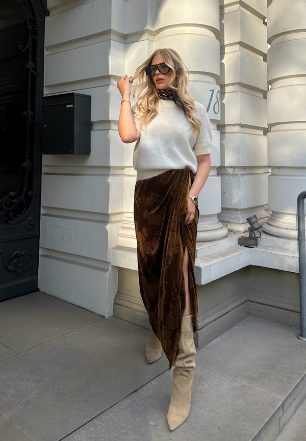 Oversized grijze gebreide trui, bruine fluwelen rok met bloemenpatroon en hoge split tot boven de dij, beige losse enkellaarsjes, grote zwarte zonnebril.
