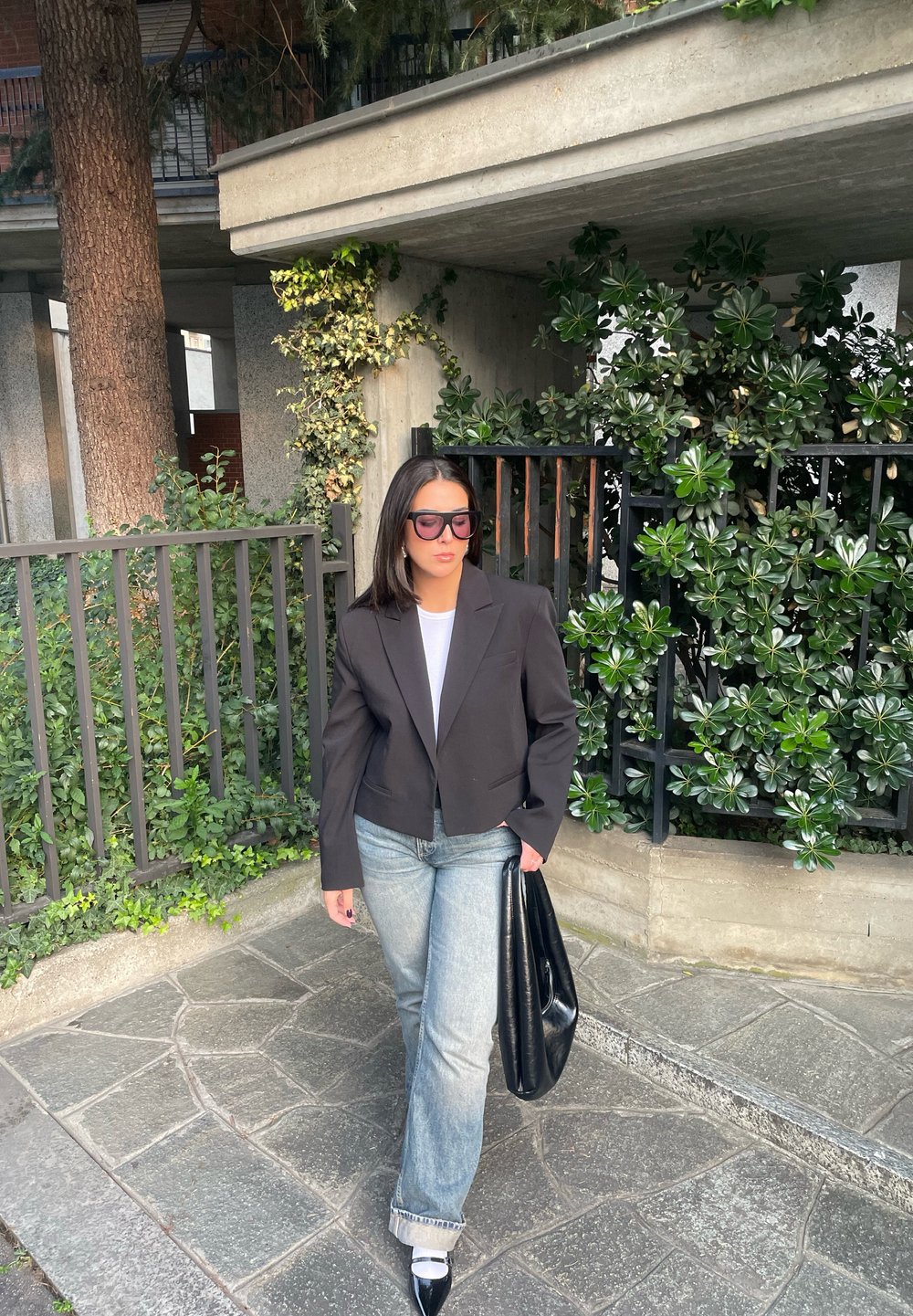 Μαύρο κομμένο σακάκι πάνω από λευκό τοπ, συνδυασμένο με ανοιχτό μπλε τζιν ευθείας γραμμής. Μαύρη τσάντα χειρός και γόβες με μυτερή μύτη ολοκληρώνουν το στυλ.