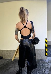 Μαύρο χωρίς μανίκια body που έχει ανοιχτή πλάτη, συνδυασμένο με ψηλόμεσα, φαρδιά δερμάτινα σορτς. Τα αξεσουάρ περιλαμβ�άνουν μια μικρή μαύρη τσάντα.