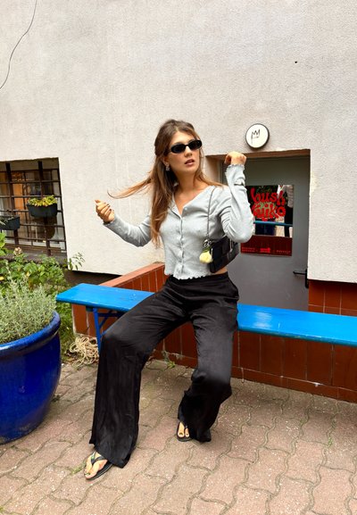 Cardigan gris acanalado con cierre de botones, pantalones de pierna ancha negros y chanclas negras. Los accesorios incluyen un bolso pequeño y gafas de sol.