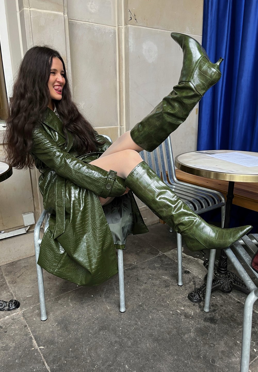 Grüner Trenchcoat aus leder mit Krokodilprägung, kombiniert mit passenden kniehohen Stiletto-Stiefeln, die eine glänzende Textur und spitze Zehen aufweisen.