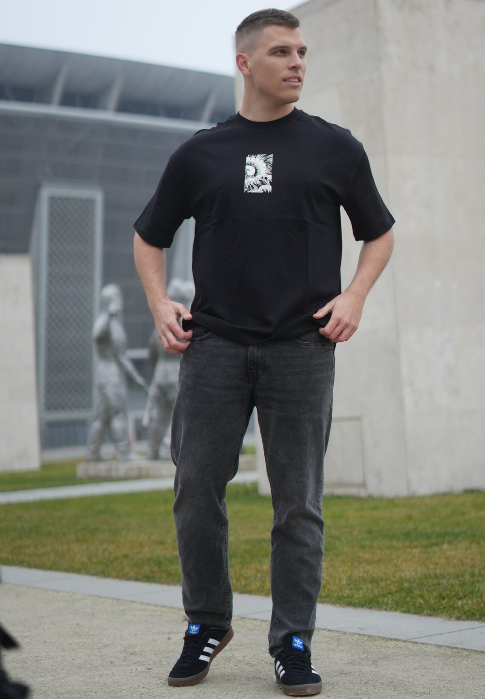 T-shirt noir à manches courtes avec un imprimé graphique au centre, associé à un jean gris foncé et des baskets noires avec des accents bleus.