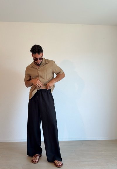 Camisa de manga corta beige, pantalones negros sueltos con cinturilla elástica y chanclas marrones. Texturas sencillas y colores neutros sobre un fondo claro.