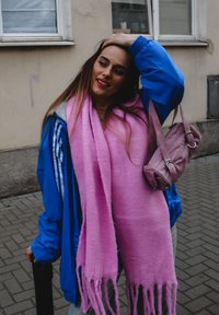 Μπλε αθλητική ζακέτα, ροζ κασκόλ και μικρή δερμάτινη τσάντα. Φόντο με πέτρινη επιφάνεια και παράθυρο. Το κασκόλ έχει φούντες στις άκρες.