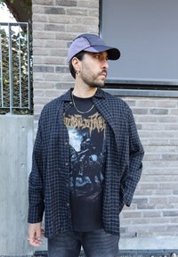 A black checkered button-up shirt layered over a graphic black t-shirt featuring gold lettering. Paired with grey jeans and a navy and grey cap worn backwards.