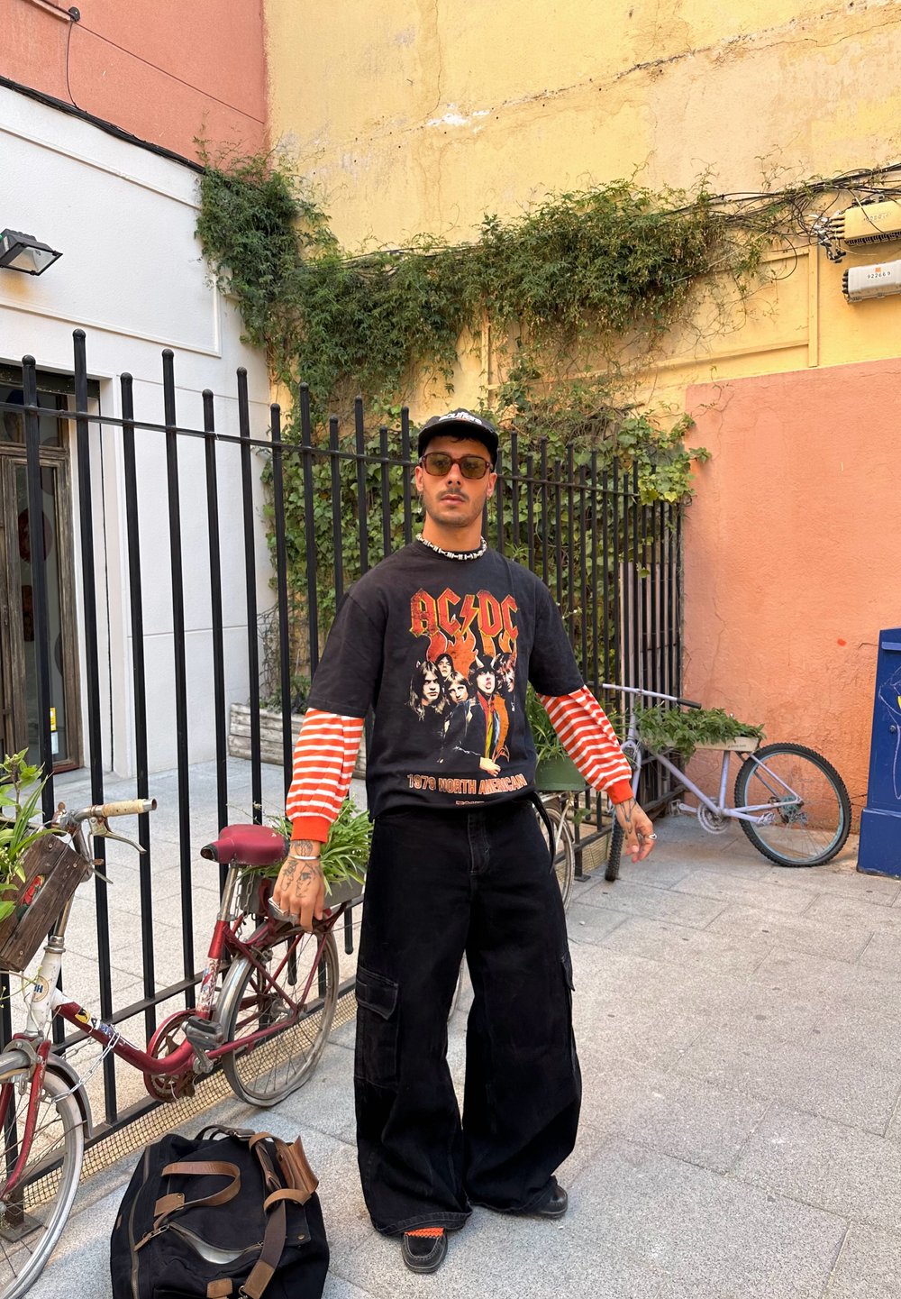 Sweatshirt oversized preto com gráfico da AC/DC, com mangas listradas em vermelho e branco, combinado com calças largas pretas e sapatos de plataforma pretos.