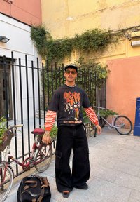 Sweatshirt oversized preto com gráfico da AC/DC, com mangas listradas em vermelho e branco, combinado com calças largas pretas e sapatos de plataforma pretos.