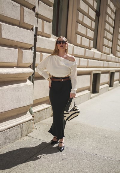 Blusa blanca sin mangas, falda larga negra, zapatos negros y un bolso de mano con estampado de cebra. Una pulsera dorada y gafas de sol oscuras completan el look.