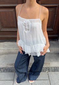 Balta be rankovių palaidinė su volaniniu kraštu, turinti susiraukšlėjusį priekį ir nėriniuotą apdailą. Derinama su tamsiomis džinsinėmis platėjančiomis kelnėmis. Paprasti aksesuarai.