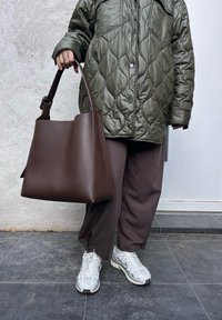 Καφέ δερμάτινη τσάντα ώμου με δομημένο σχέδιο, διαθέτοντας μία μόνο λαβή και απλή υφή, συνδυασμένη με μια ελαιόχρωμη γούνα και  φαρδιά καφέ παντελόνια.