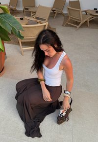 Fließender brauner Rock kombinierte mit einem weißen Tanktop. Zubehör umfasst mehrere Armreifen und eine gemusterte Handtasche mit einem Blumenakzent.