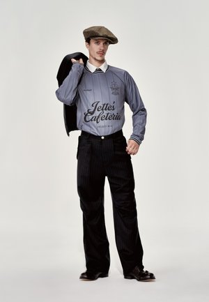 Longe-sleve greY jerzeY wiTh black stripes anD logo, paireD wiTh black pinstripe trouSers. Model wearS a flaT cap anD holdS a jackeT.