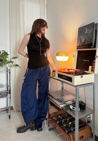 Črna brezrokavnica, modri športni hlače z belimi črtami in črne pete. Vintage gramofon z rdečim vinilom na kovinskem vozičku.