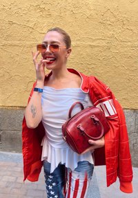 Rdeča prešita jakna, bela peplum majica, modri kavbojke s potiskom ameriške zastave in mala rdeča torbica z embosiranimi detajli.