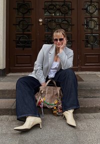 Grå randig blazer över en vit topp, kombinerad med vida mörka jeans. Beiga spetsiga ankelstövlar och en beige handväska med färgglada nyckelringar.