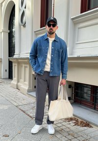 Jeansjacka, vit tröja, gråbyxor och vita sneakers. Håller en beige tote-väska. Utomhusmiljö med stengång.