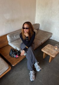 Czarny długi rękaw bluzka i szare spodnie noszone z szarymi butami sportowymi. Obecna jest czarna torebka z akcentami oraz drewniany stół z świeczką.