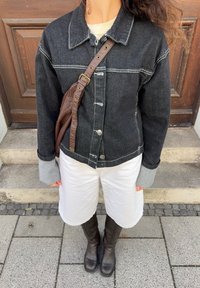 Črna denim jakna s srebrnimi gumbi, sivi manšeti, oblečena čez bele kratke hlače. Rjava usnjena torba z nastavljivim trakom. Črne škornje do kolen.