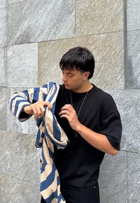 Svītraini smilšu un zili audumi, ko tur persona, ar brīvu dizainu. Personai ir mugurā melna krekls un vienkārša sudraba kaklarota.