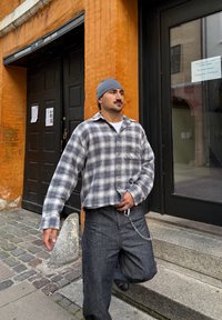 Geruite flanellen blouse in blauw, crème en zwart, gecombineerd met donkere spijkerbroek. Kleding heeft een cropped ontwerp en een kettingaccessoire.