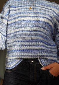 Blå og hvitstripet strikkegenser med løs passform og ribbestruktur, kombinert med mørke denimjeans, som viser en avslappet stil.