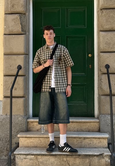 Camisa de cuadros de manga corta en verde y blanco, pantalones cortos de denim holgados, zapatillas negras con rayas blancas y un bolso cruzado negro. Fondo de puerta verde.