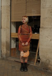 Sukienka bodycon w gradientzie od pomarańczowego do czerwonego, z czarnymi detalami w postaci uprzęży. Czarne botki na platformie i pomarańczowa torebka na ramię z puszystym akcentem.
