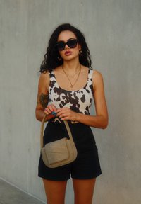 Μπλουζάκι με σχέδιο αγελάδας σε άσπρο και μαύρο, μαύρο σορτσάκι ψηλής μέσης και μικρή μπεζ τσάντα χεριού, αξεσουάρ με γυαλιά ηλίου και κοσμήματα.