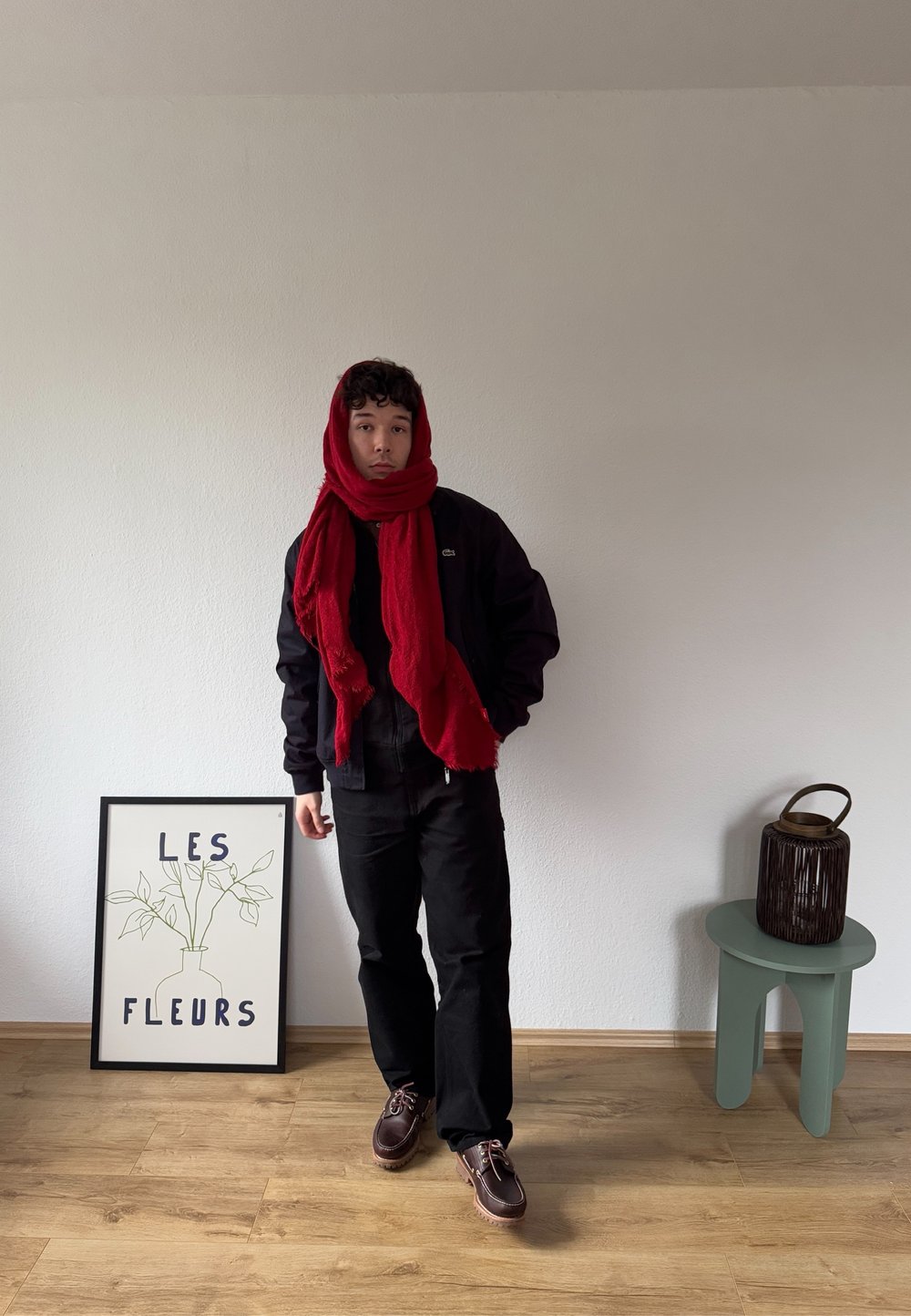Črna jakna in hlače, rdeč šal, rjave čevlje. Zelen stranski tabel s pleteno košaro. Okvirjena umetnost z besedilom "LES FLEURS" in načrtom rastline.
