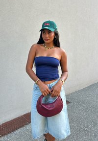 Mornarska brezramna majica, svetlo modri jeans kratke hlače, zelena kapa z motivom češnjev, in maroon hobo torba. Podrobnosti vključujejo zlate nakit in perlico ogrlico.
