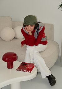 Κόκκινο πουλόβερ πάνω από ένα ανοιχτό γκρι γιλέκο, λευκά παντελόνια, μαύρες μπότες. Μια στρογγυλή, κόκκινη επιτραπέζια λάμπα και ένα περιοδικό σε ένα λευκό τραπέζι. Μαλακό καναπέ με στρογγυλά μαξιλάρια.