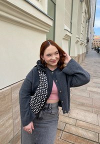 Grå ullcardigan med knapper, rosa kort topp, høy midje grå denimskjørt, og en svart veske med sølvnitter og en bue som detalj.