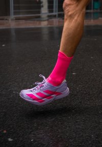 Futó alsó lába �élénk rózsaszín zoknival és fehér cipővel, pink csíkokkal, félúton a nedves járdán.