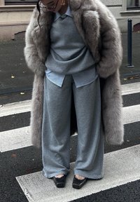 Sivý sveter a široké nohavice vrstvené cez pruhované tričko, doplnené dlhým, mäkkým sivým kožušinovým kabátom. Čierne topánky s mašličkovými detailmi.