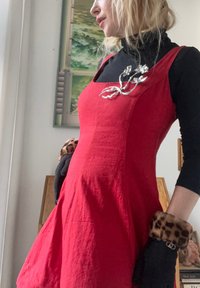 Rochie roșie, fără mâneci, cu o suprafață texturată, având o broșă florală argintie. Asortată cu mănuși negre, decorate cu imprimeu de leopard.