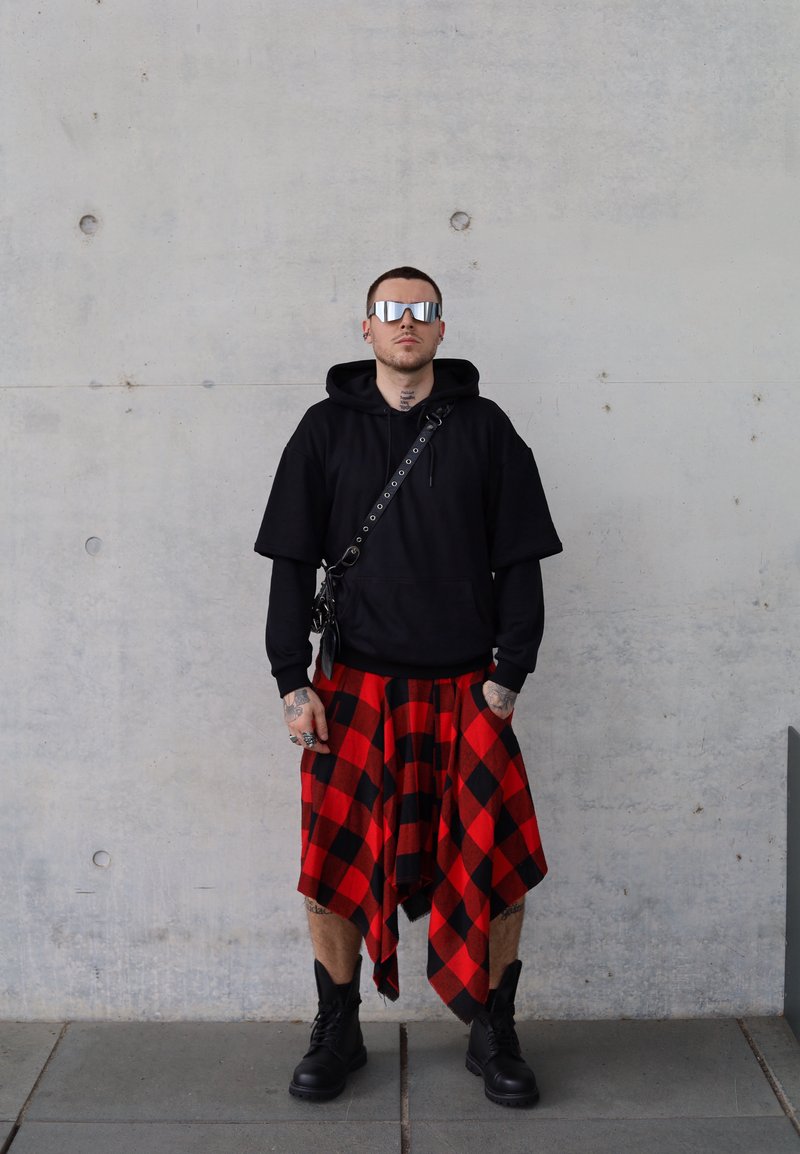 Μαύρη oversized φούτερ, κόκκινη και μαύρη καρό φούστα και μαύρες αρβύλες. Γυαλιά ηλίου με αντανάκλαση και αξεσουάρ συμπληρώνουν το σύνολο.