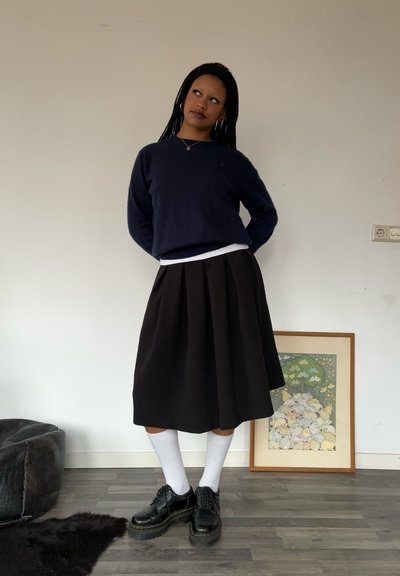 Suéter navy, camiseta blanca, falda negra con plisados, calcetas blancas hasta la rodilla, zapatos negros. Trenzas cortas y aretes de aro dorados.