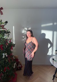 Vestito senza maniche a quadri neri e rossi con orlo trasparente, abbinato a una fascia per capelli. Sullo sfondo, un albero di Natale decorato e giocattoli.