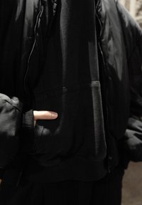 Juoda pūkinė striukė su užtrauktuku, ribinėmis apykaklėmis ir priekinė kišene. Audinys turi lygų paviršių ir yra šiek tiek blizgus.