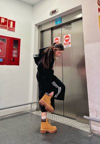 Hnedé semišové platformové čižmy so žltými šnúrkami, hnedým akcentom na vrchu a hrubou, masívnou podrážkou. Čierne nohavice s bielymi pruhmi.