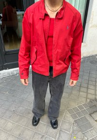 Κόκκινη ελαφριά ζακέτα με υψηλό λαιμό, συνδυασμένη με κόκκινο τιραντάκι, μαύρα φαρδιά τζιν και μαύρα δερμάτινα παπούτσια, με ορατό λογότυπο.